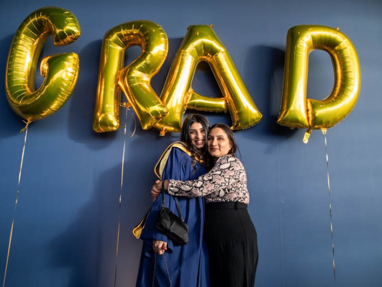 Graduate is hugged by family member under golden GRAD balloons