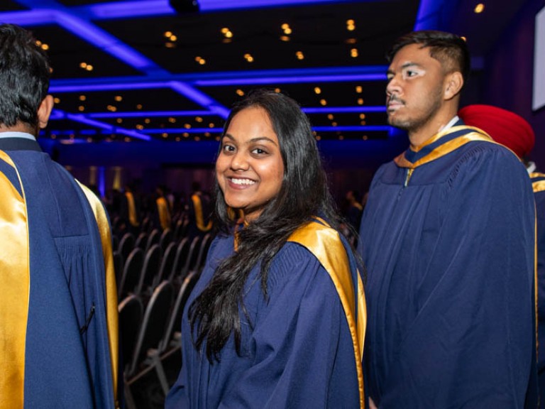 Graduate smiles at camera as they proceed in line