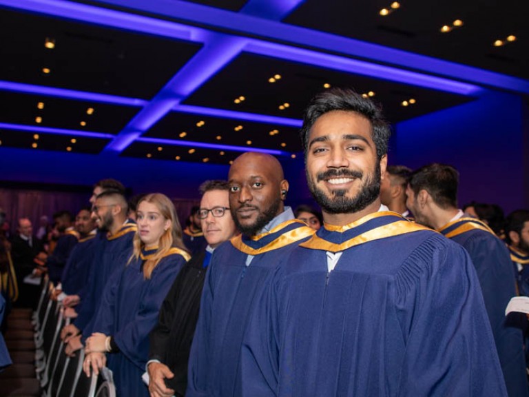 Graduates standing in ceremony hall look at camera