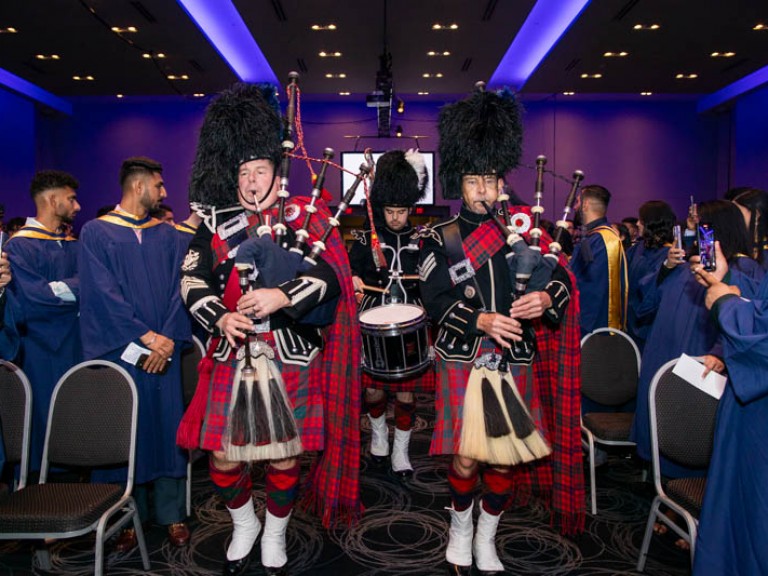 People in Scottish regalia playing bagpipes proceed down aisle