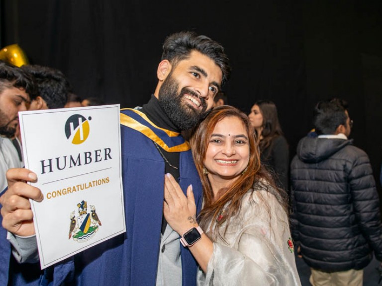 Graduate hugs ceremony guest with congratulations paper