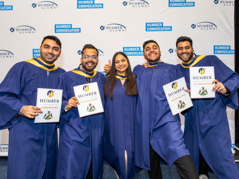 Five graduates pose for photo in front of Humber convocation wall