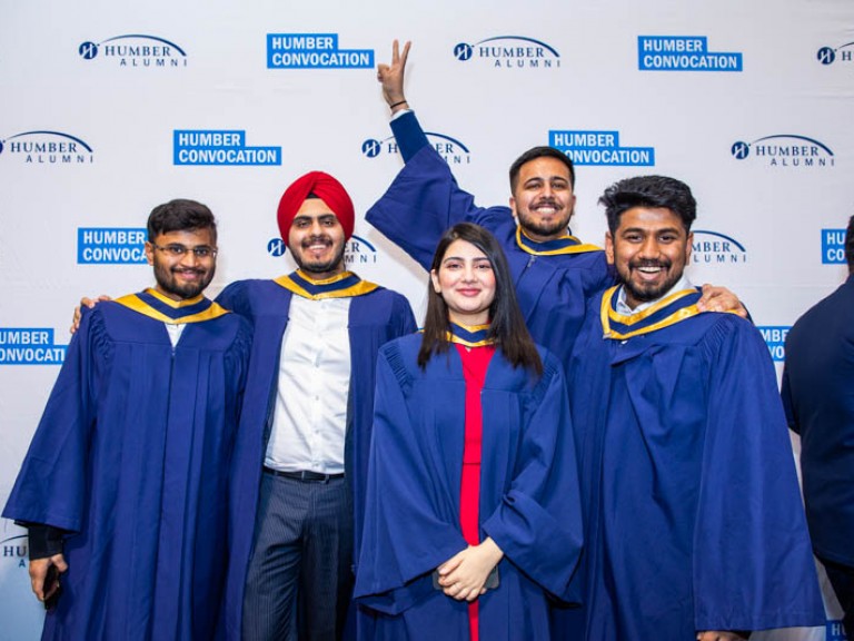 Five graduates pose in front of Humber Convocation wall