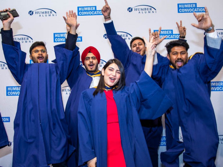 Five graduates make excited poses with arms up for photo