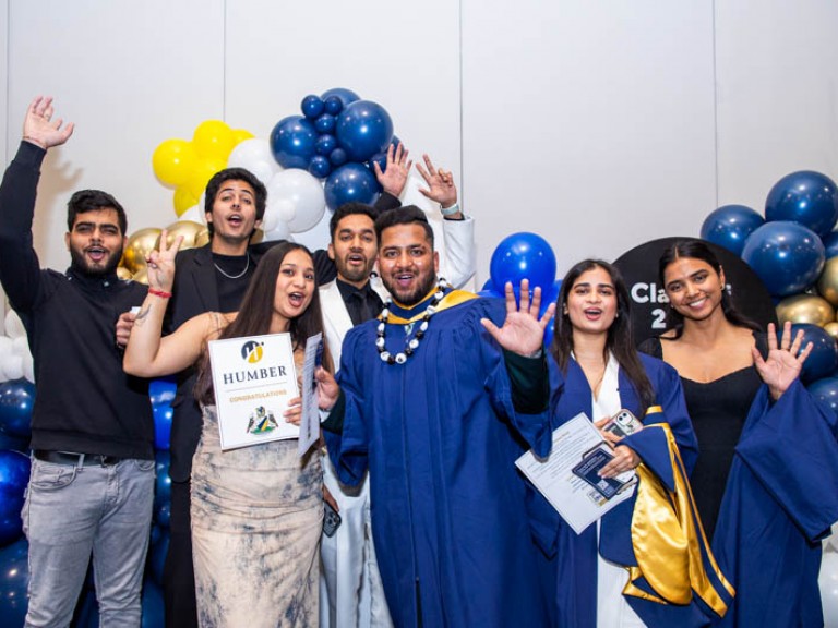 Two graduates pose with five guests in front of blue balloons