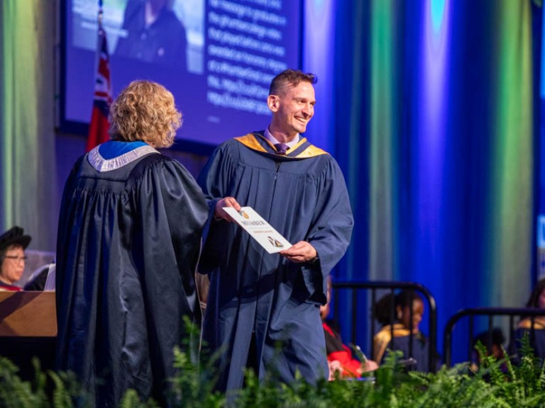 Graduate on stage smiling towards audience