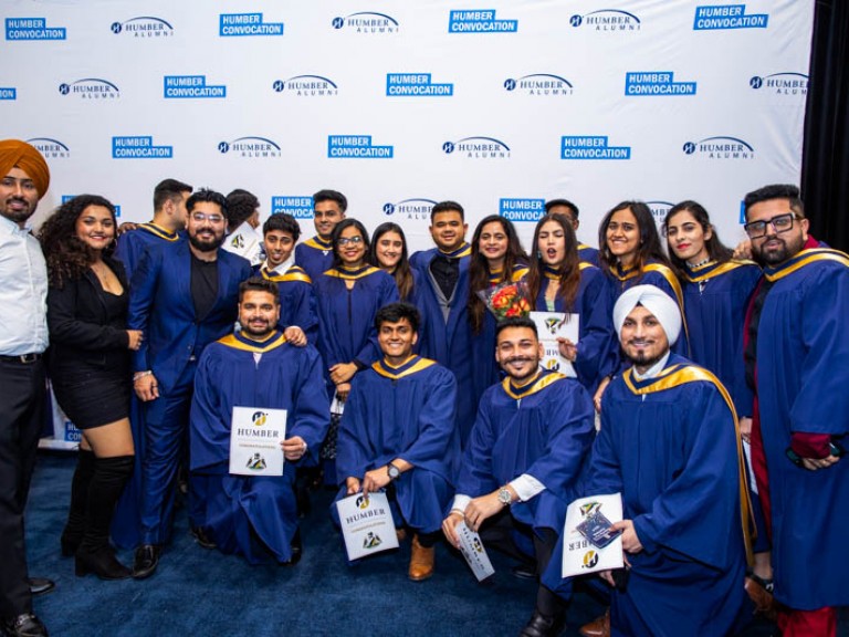 Large group of graduate pose for photo in front of Humber Convocation wall