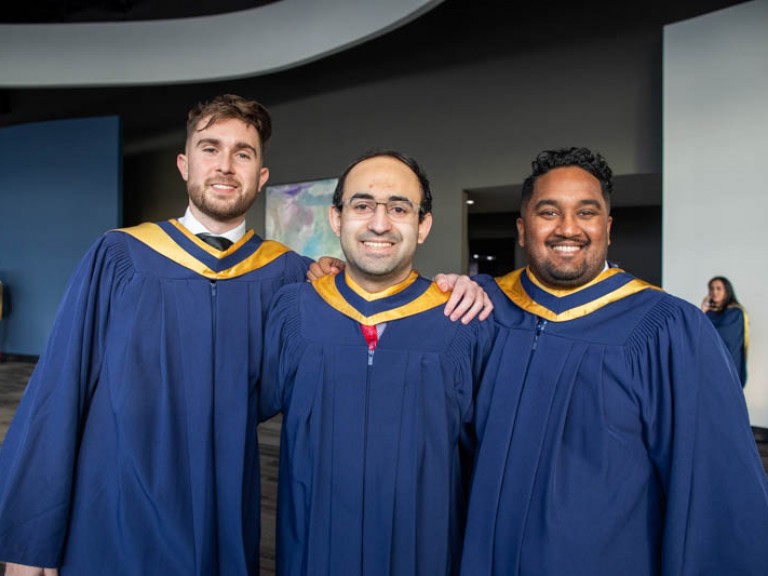 Three graduates posing with arms around each other