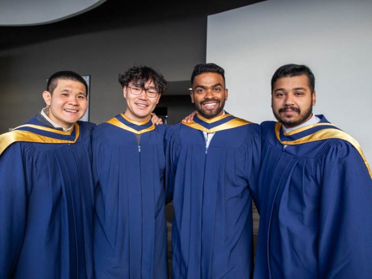 Four graduates posing for photo with arms around each other