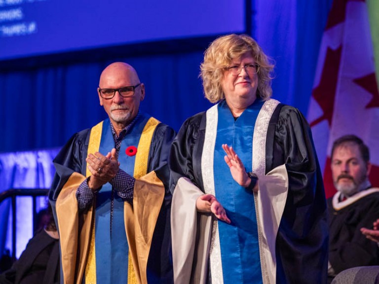 Humber president Ann Marie Vaughan standing on stage beside someone and clapping