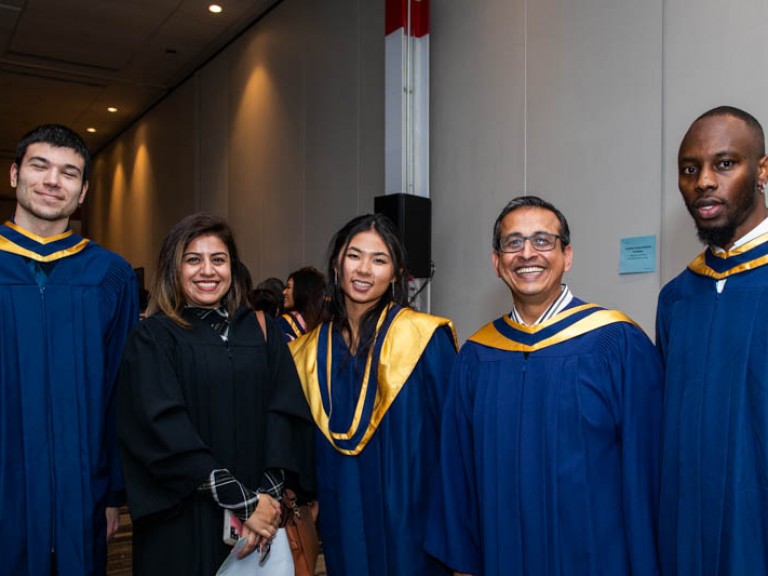 Four graduates pose with person in black robe