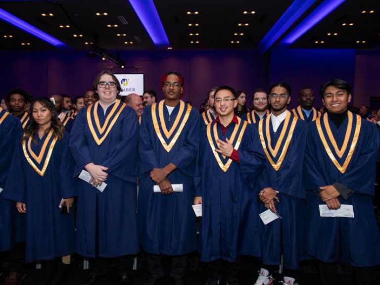 Row of graduates in ceremony hall look at camera