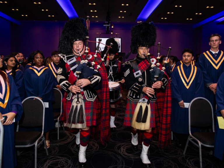People in Scottish regalia play bagpipes as they walk down aisle