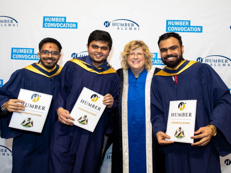 Three graduates smile for photo with Ann Marie Vaughan