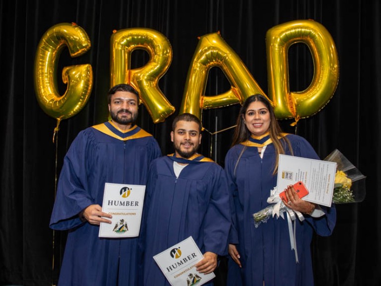 Three graduates take photo in front of gold GRAD balloons