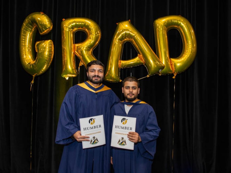Two graduates take photo in front of gold GRAD balloons 