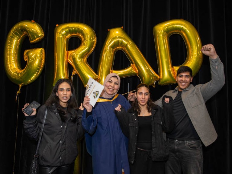 Graduate takes photo with three family members in front of gold GRAD balloons