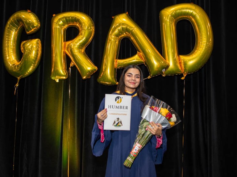 Graduate takes photo in front of gold GRAD balloons