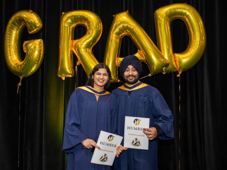 Two graduates pose in front of GRAD balloons