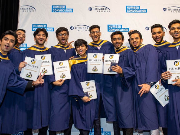 Ten graduates pose for photo in front of Humber convocation wall