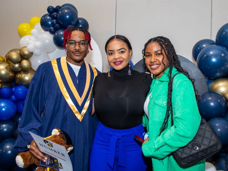 Graduate poses with two guests in front of balloons