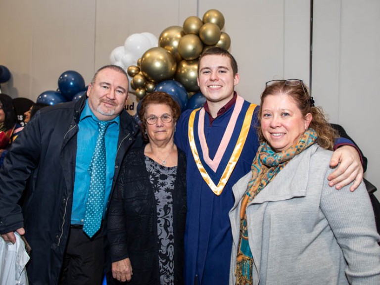 Graduate poses with three family members in front of balloons