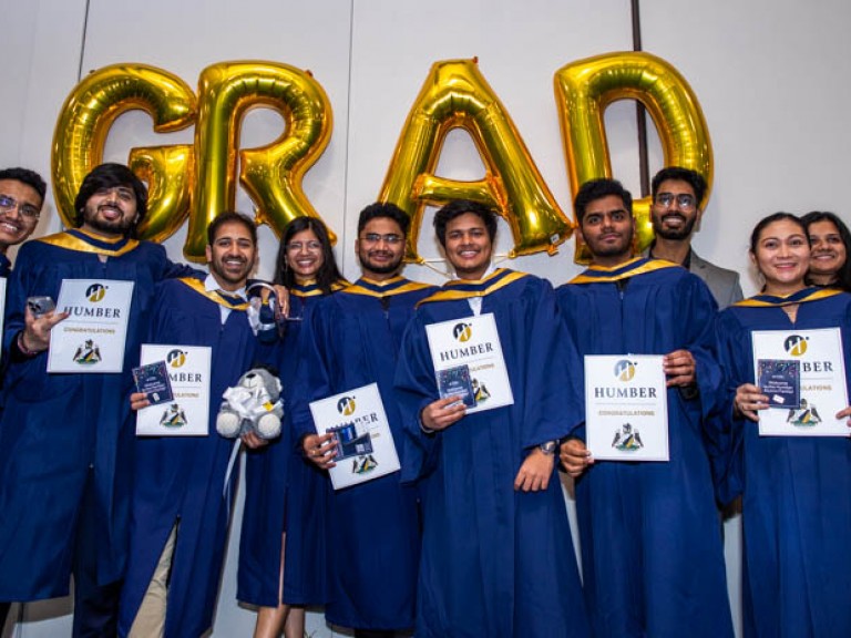 Graduates smile in front of gold GRAD balloons