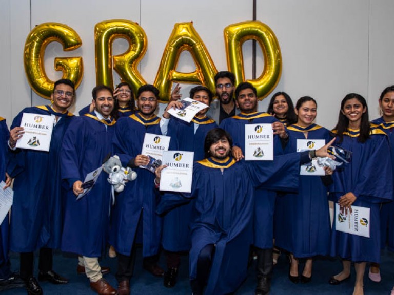 Group of graduates pose in front of GRAD balloons