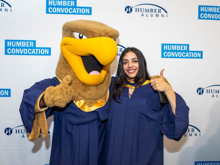 Graduate and Humber mascot make thumbs up sign