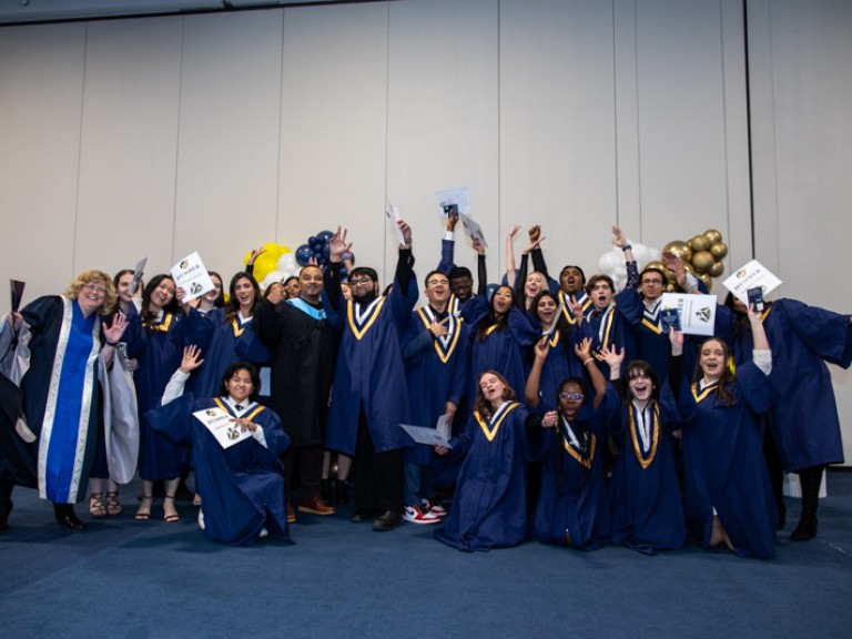 Large group of graduates raise arms in celebration