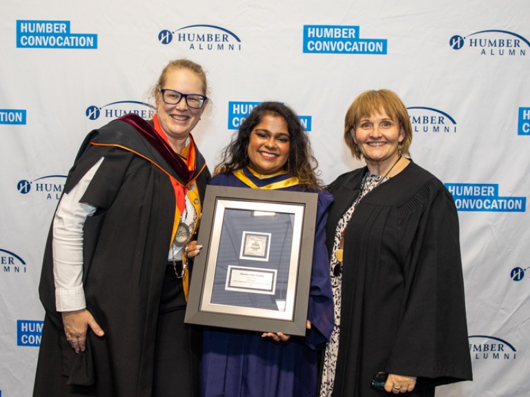 Graduate with framed award takes photo with two people in black robes
