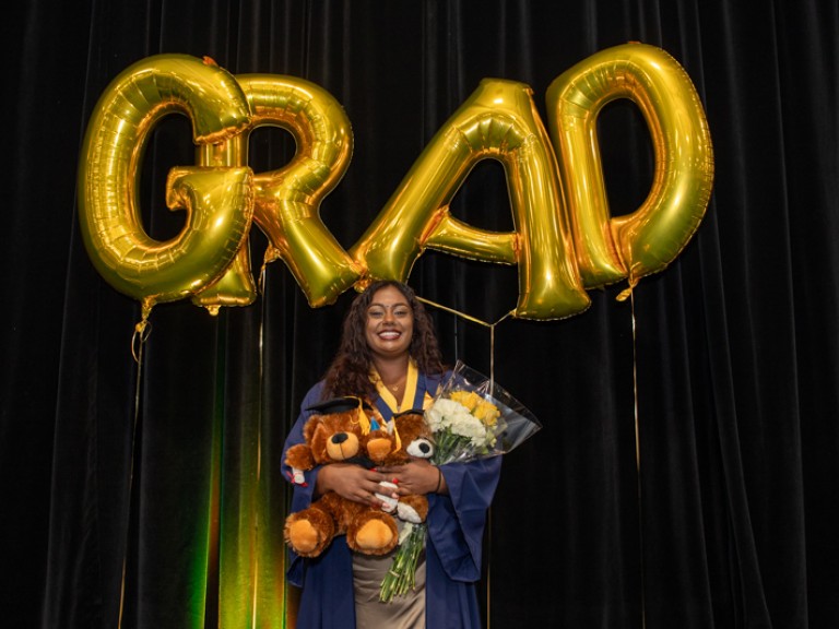 Graduate takes photo in front of GRAD balloons