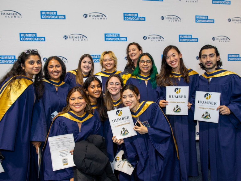 Group of graduates take photo in front of Humber convocation wall