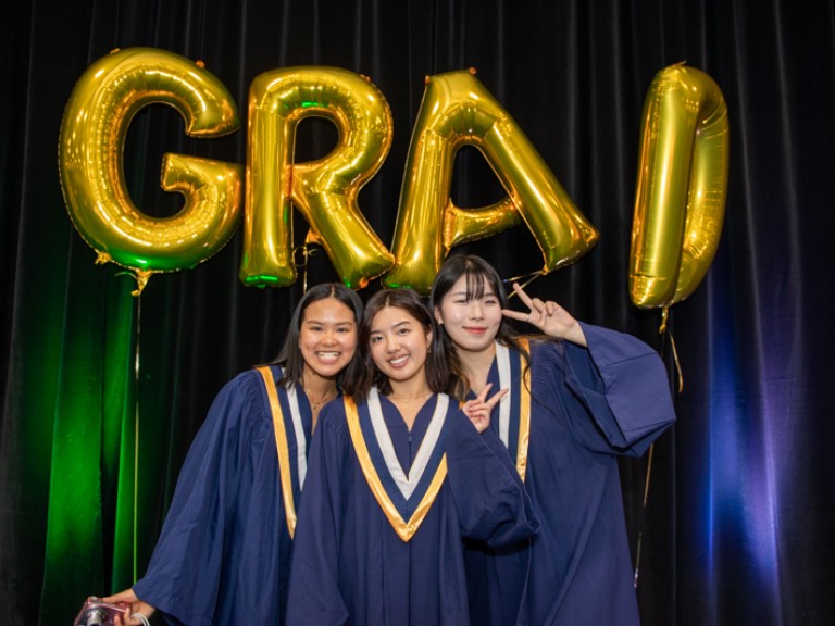 Three graduates take photo in front of GRAD balloons