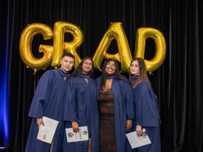 Four graduates take photo in front of GRAD balloons