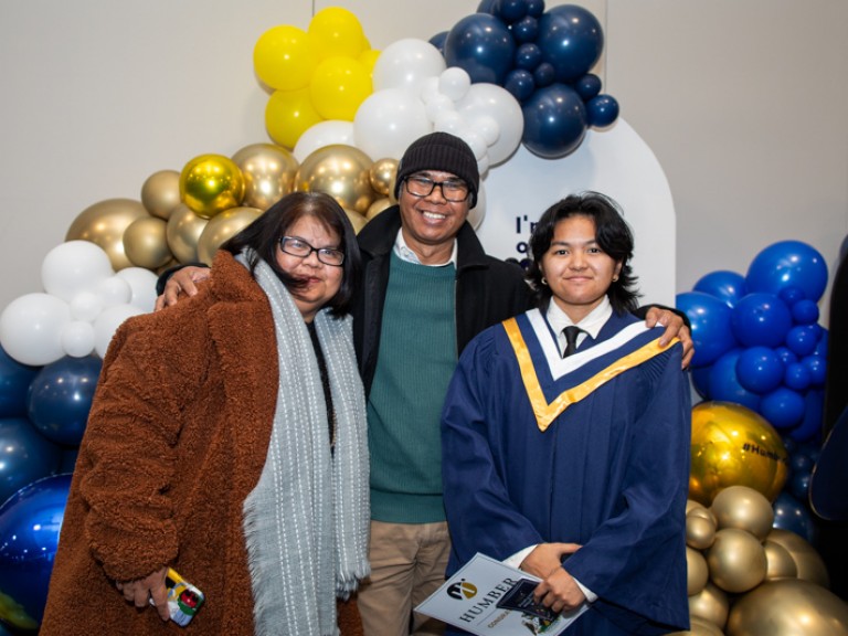 Graduate takes photo with parents in front of balloons