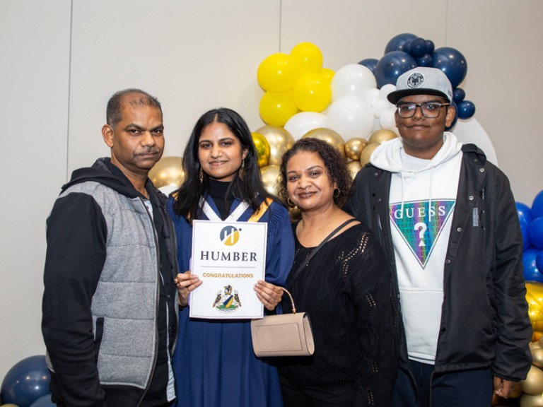 Graduate takes photo with three family members in front of balloons