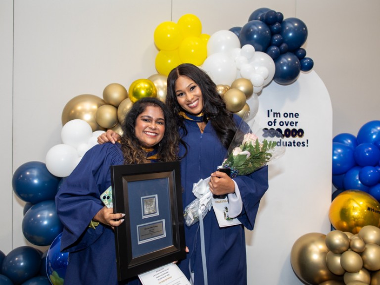 Two graduates take photo in front of balloons