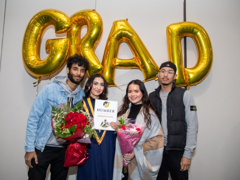 Graduate takes photo with three people in front of GRAD balloons