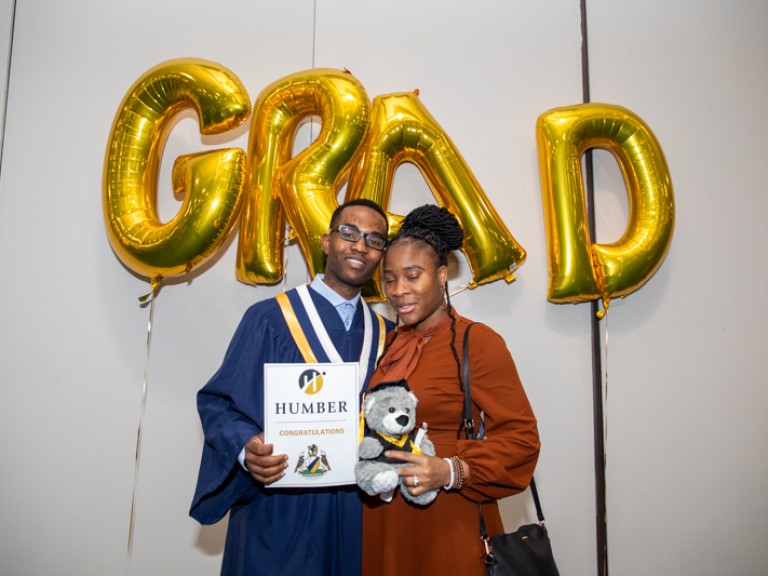 Graduate takes photo with person in front of GRAD balloons