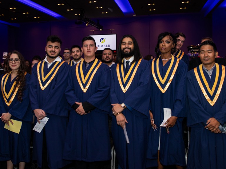 Graduates standing in ceremony hall look at camera