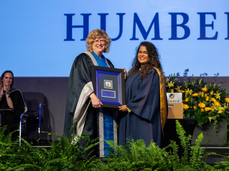 Graduate accepts framed award from Humber president