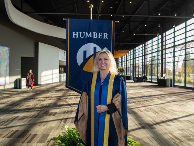 Person wearing ceremonial robe stand in front of Humber flag