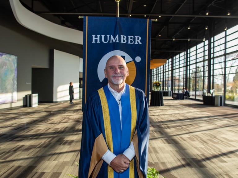 Person wearing ceremonial robe stand in front of Humber flag