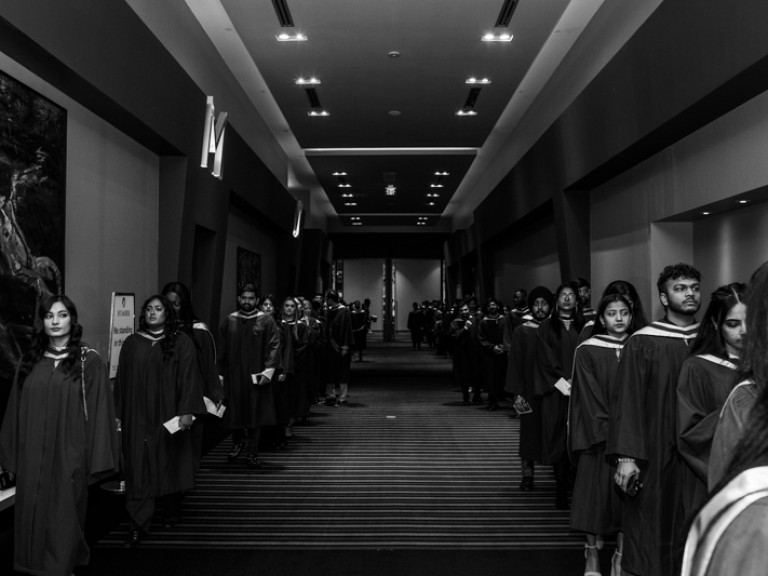Two rows of graduates lined up on both sides of a wide hallway