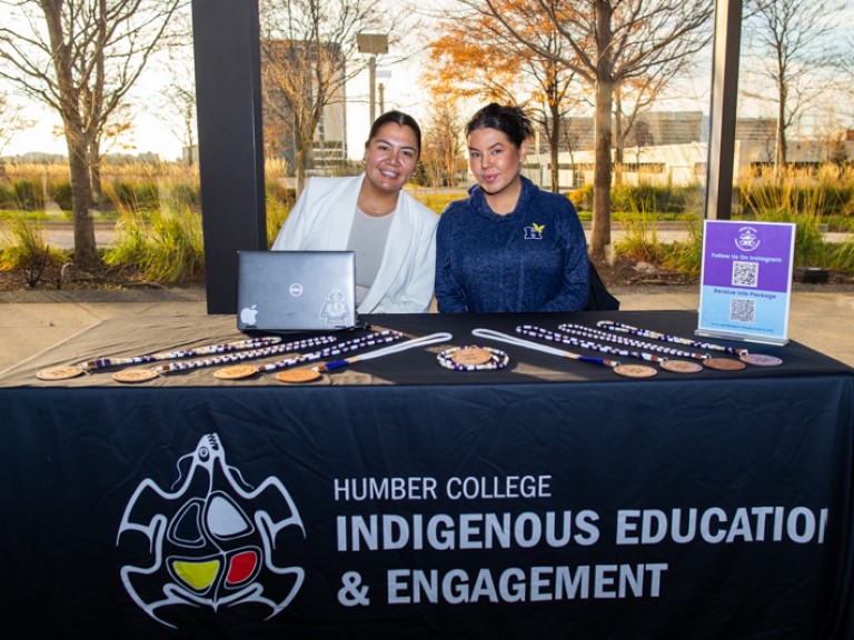 Two people sitting behind Humber College Indigenous Education & Engagement table