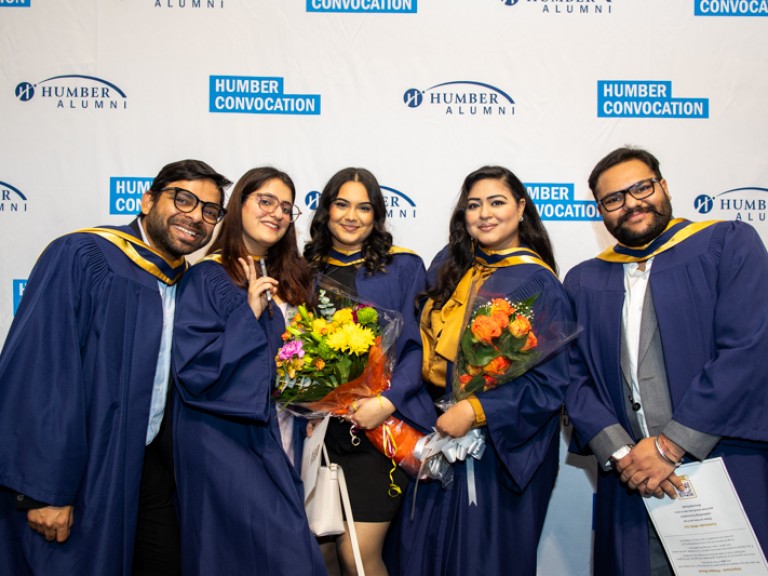 Five graduates take photo in front of Humber Convocation wall