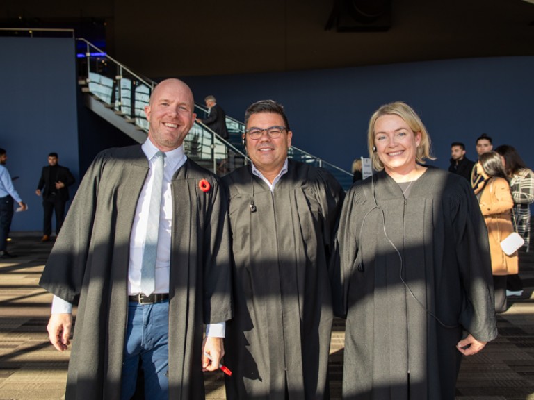 Three people in black robes smile for photo