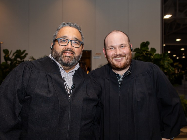 Two people in black robes pose for camera
