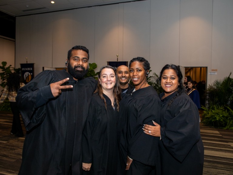 Four people in black robes smile for photo